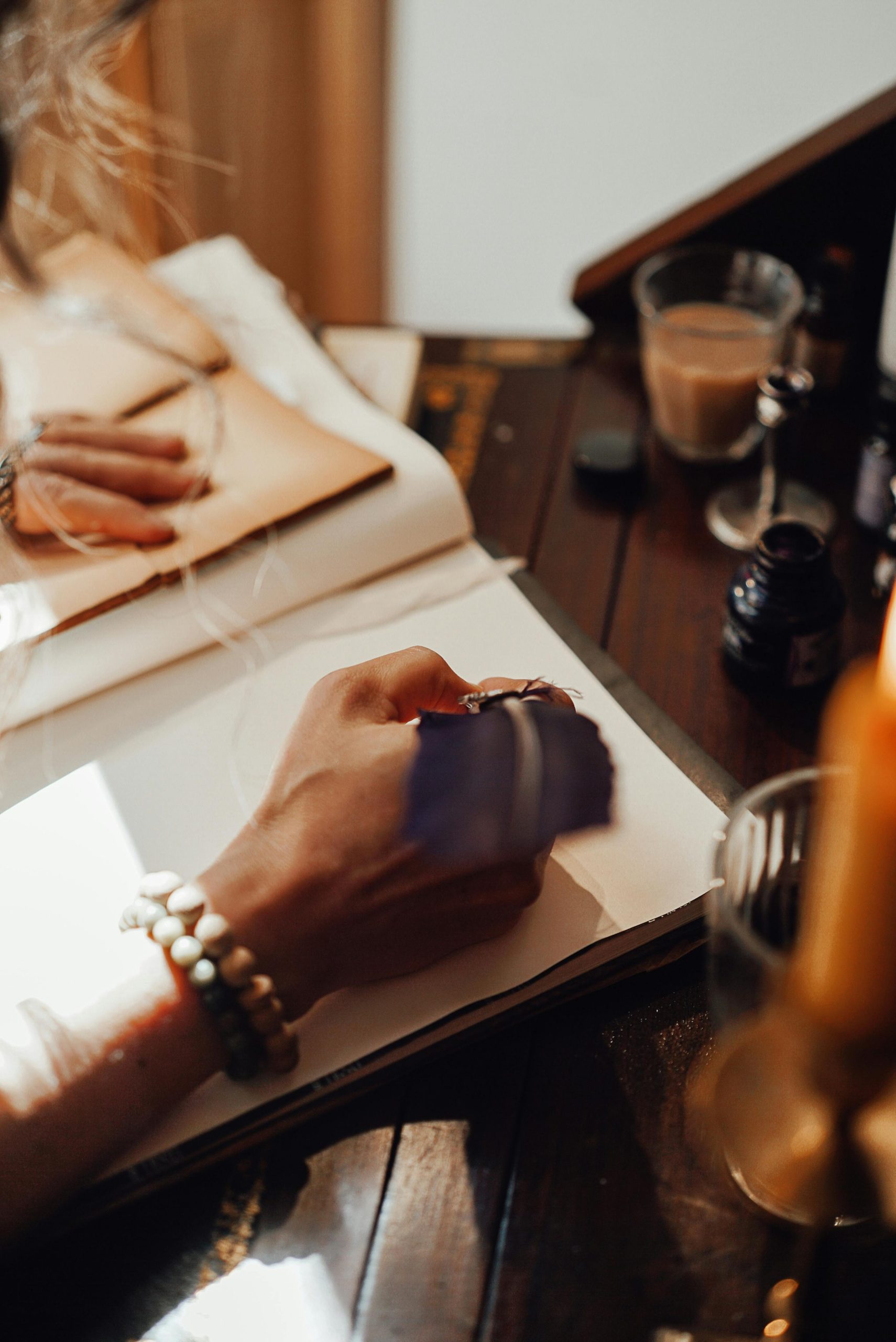 Crop anonyme d'une écrivaine prenant des notes dans un cahier avec une plume sur une table vintage à la lumière du soleil à la maison