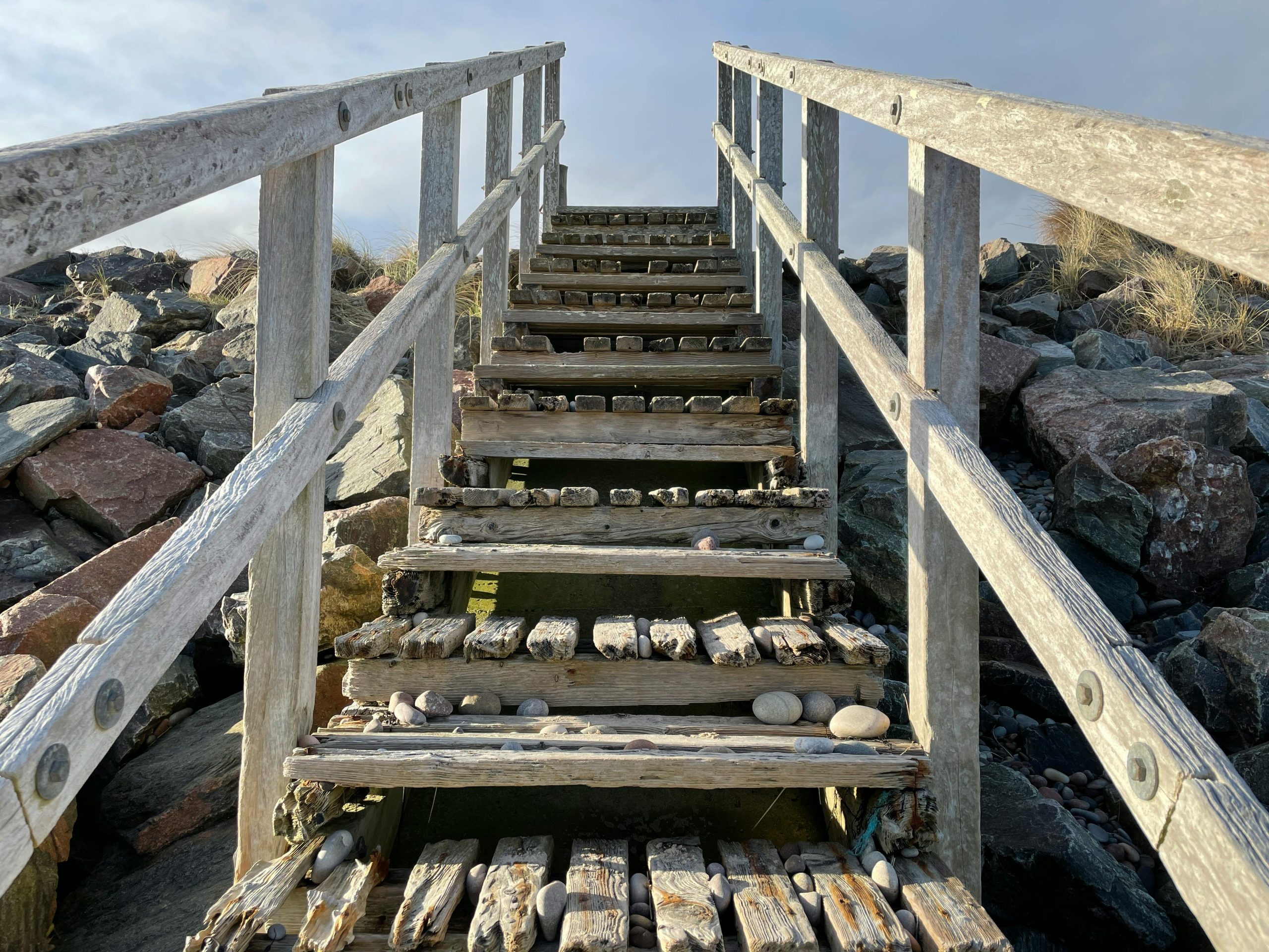 Escaliers en bois usés montant un terrain rocheux sous un ciel dégagé en Écosse.