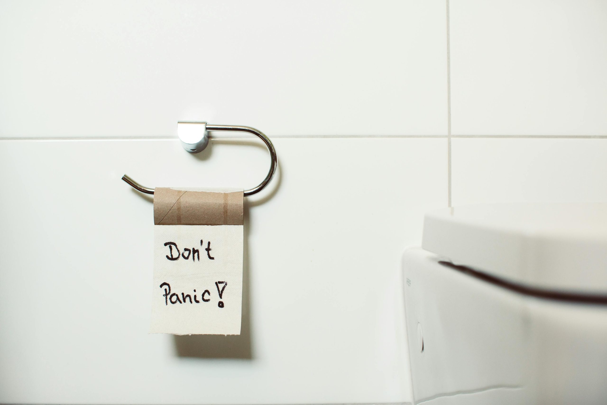Un porte-rouleau de papier toilette avec un rouleau vide affichant une note "Don't Panic !", installé dans une salle de bain moderne.