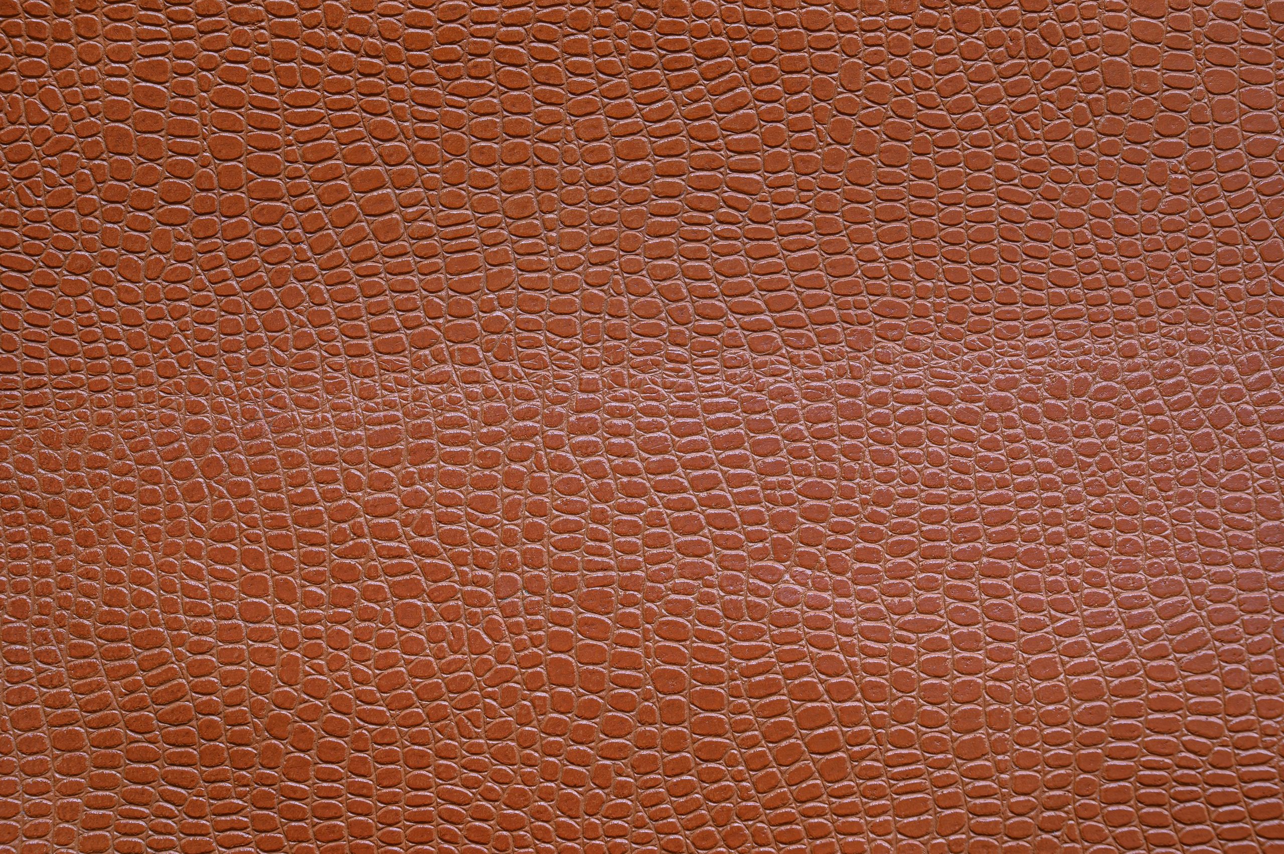 Close-up d'une surface en cuir marron texturé ressemblant à une peau de reptile, mettant en valeur des motifs complexes.