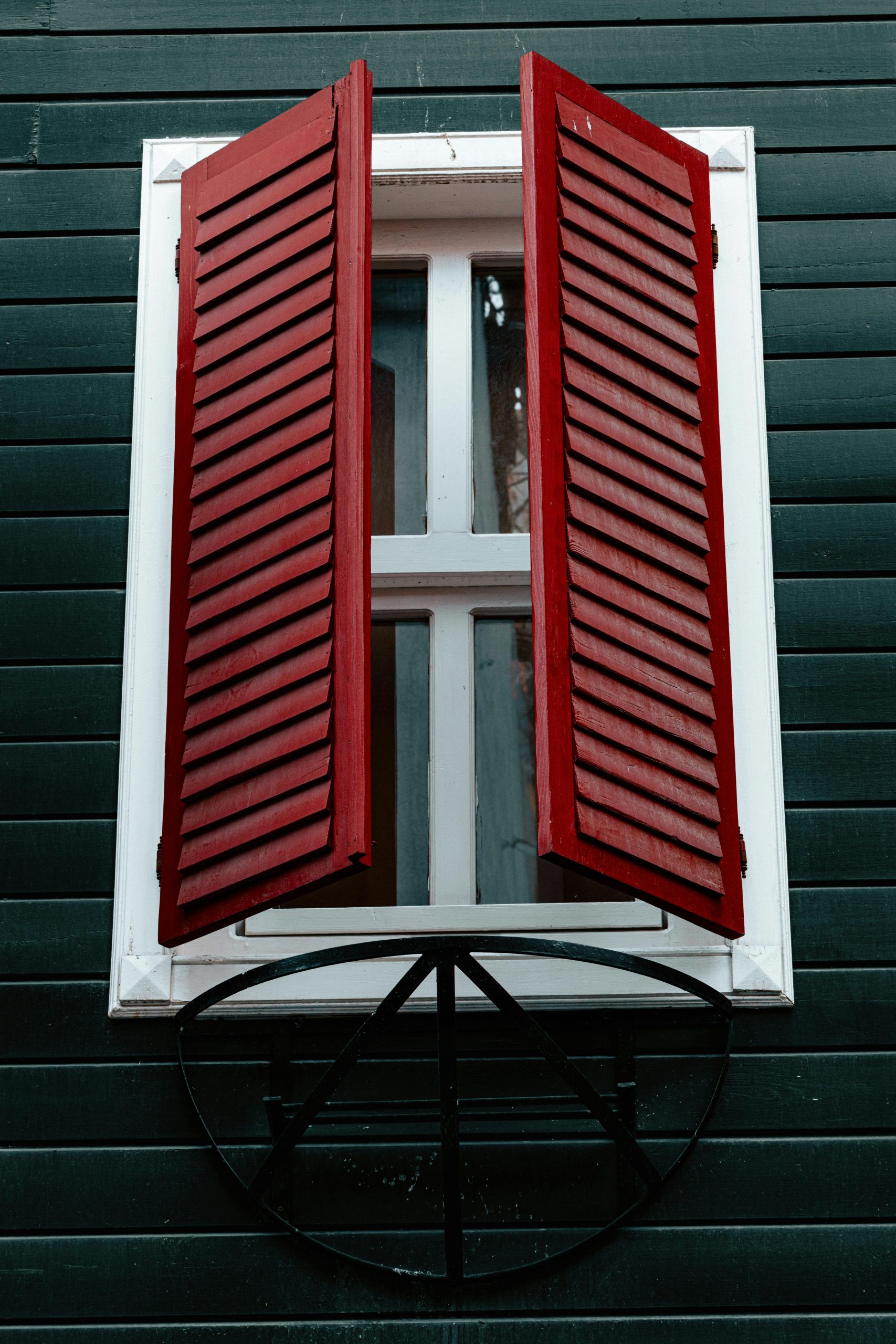 Red shutters on a green wooden wall create a striking contrast and focal point. Volets rouges sur un mur en bois vert créant un contraste et un point focal frappants.
