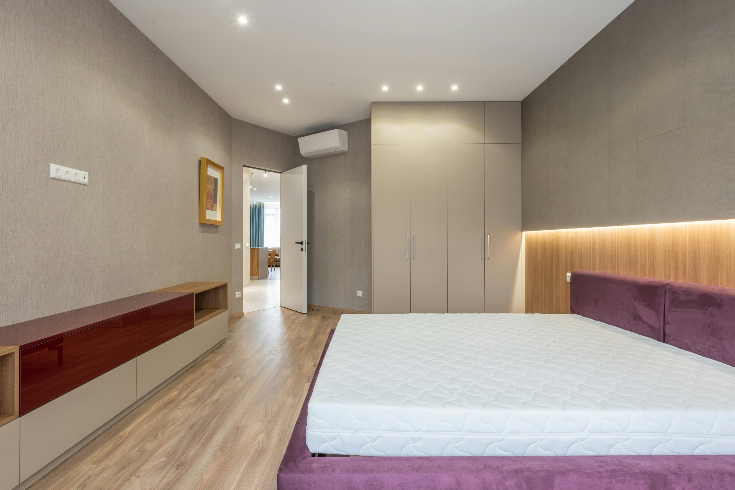 Interieur d'une chambre spacieuse et stylée avec un matelas blanc sur un lit placé contre une armoire près d'une garde-robe et une porte ouverte dans un appartement