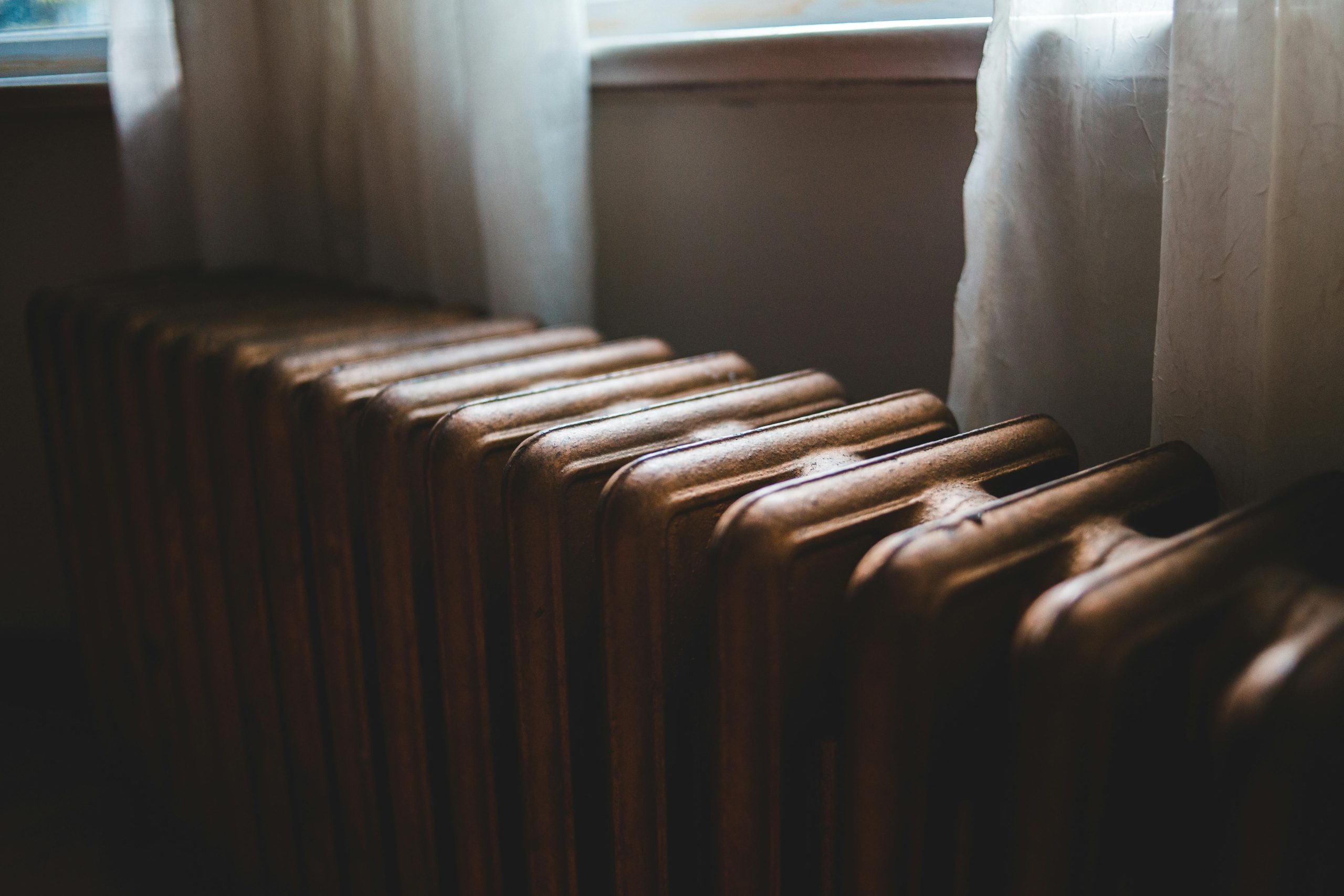 Radiateur de chauffage ancien en fonte près du rebord de fenêtre avec rideaux dans une maison