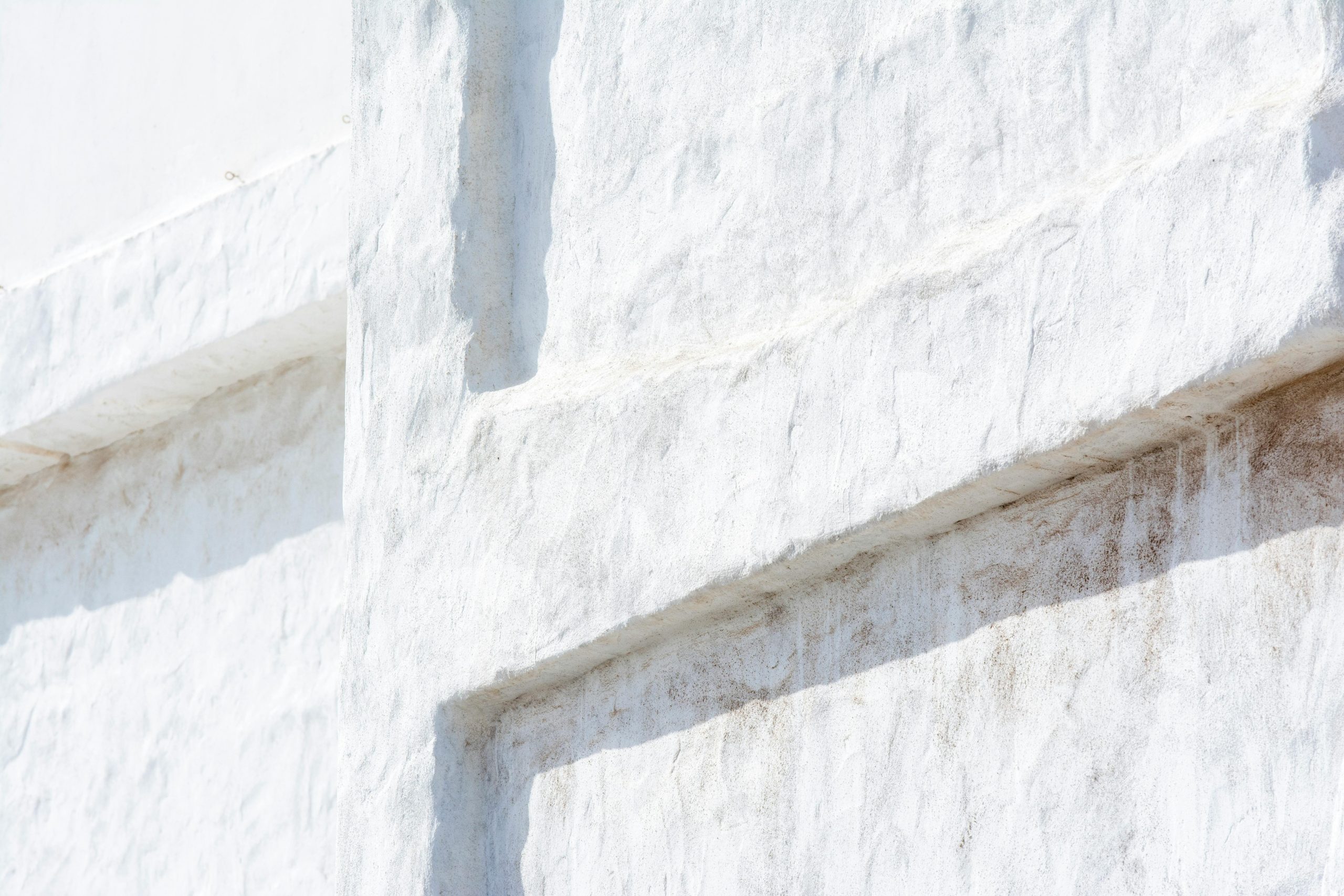 Close-up of a textured white stucco wall with a minimalist abstract design. Gros plan d'un mur en stuc blanc texturé avec un design abstrait minimaliste.