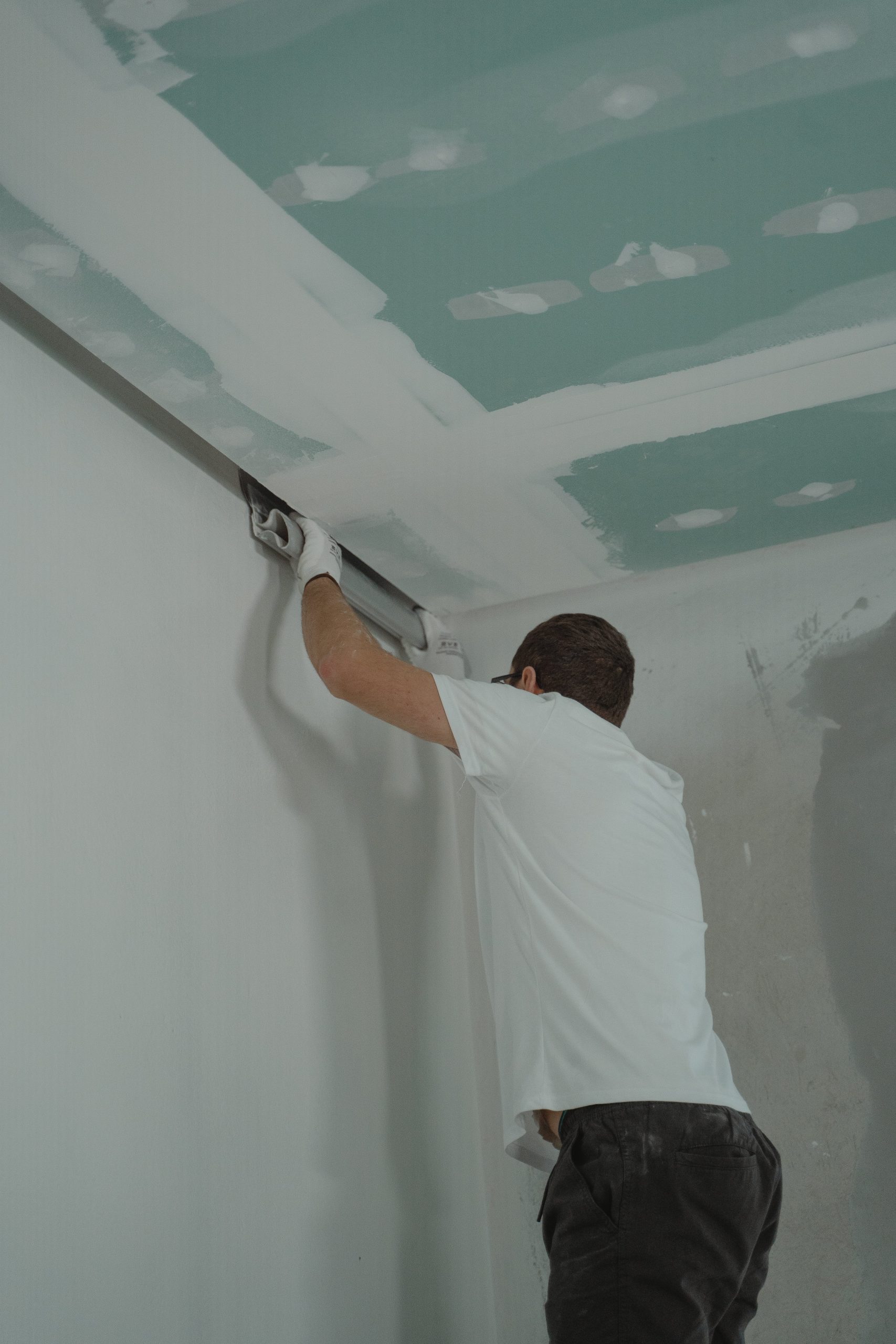 A man works meticulously on drywall installation during a house renovation. Un homme travaille méticuleusement à l'installation de cloisons sèches lors d'une rénovation domiciliaire.