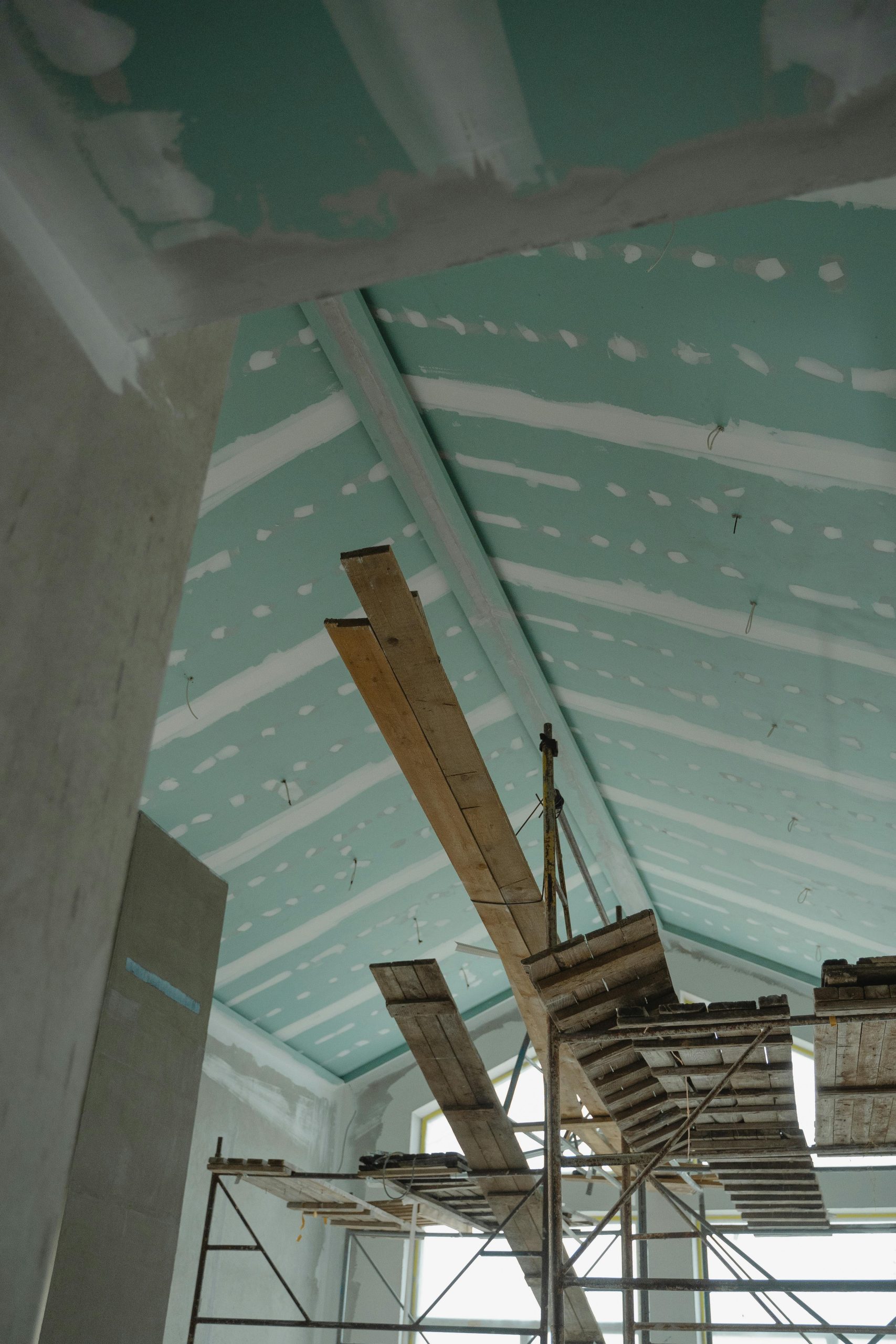 Scaffolding setup in an interior construction space with suspended ceiling boards and wooden planks. Mise en place d'échafaudages dans un espace de construction intérieur avec des panneaux de plafond suspendus et des planches en bois.