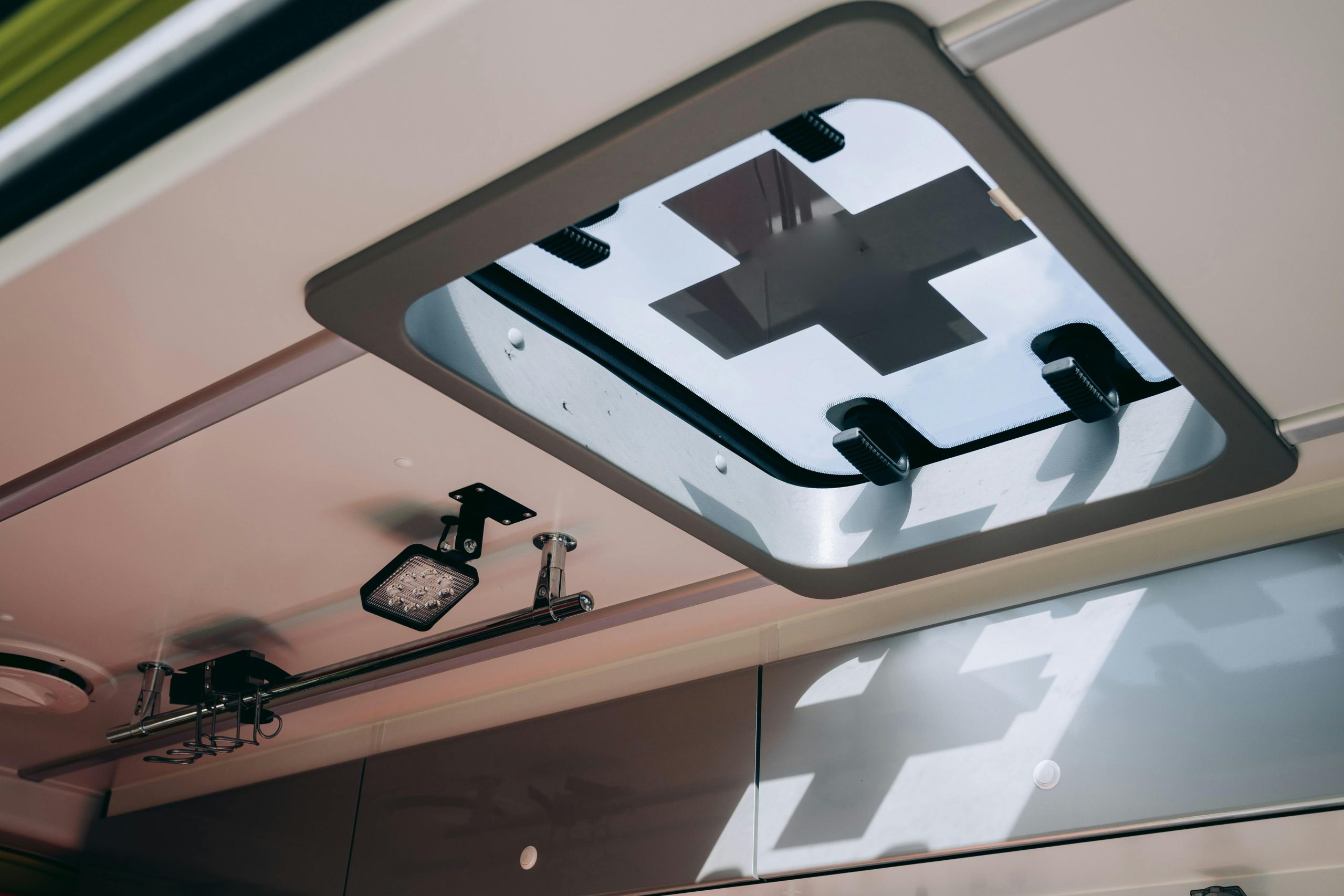 View of an ambulance's roof window featuring a medical cross symbol and ceiling equipment. Vue de la fenêtre de toit d'une ambulance présentant un symbole de croix médicale et des équipements de plafond.