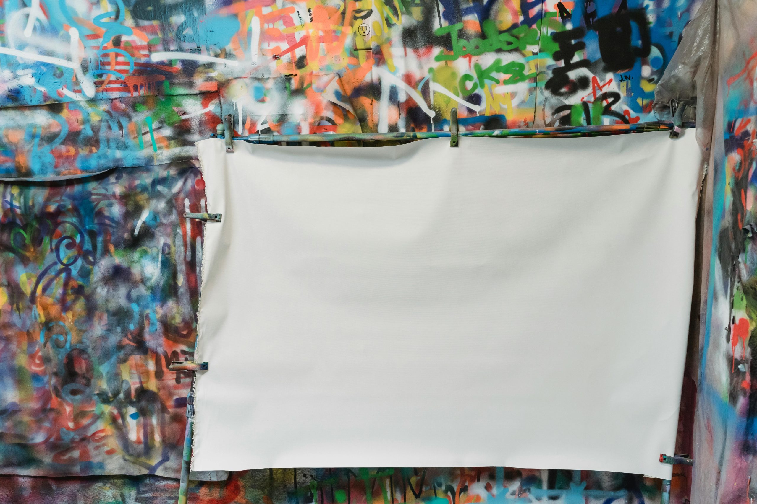 A vibrant graffiti wall with a blank white canvas in front for creative projects. Un mur de graffitis vibrants avec une toile blanche vierge devant pour des projets créatifs.