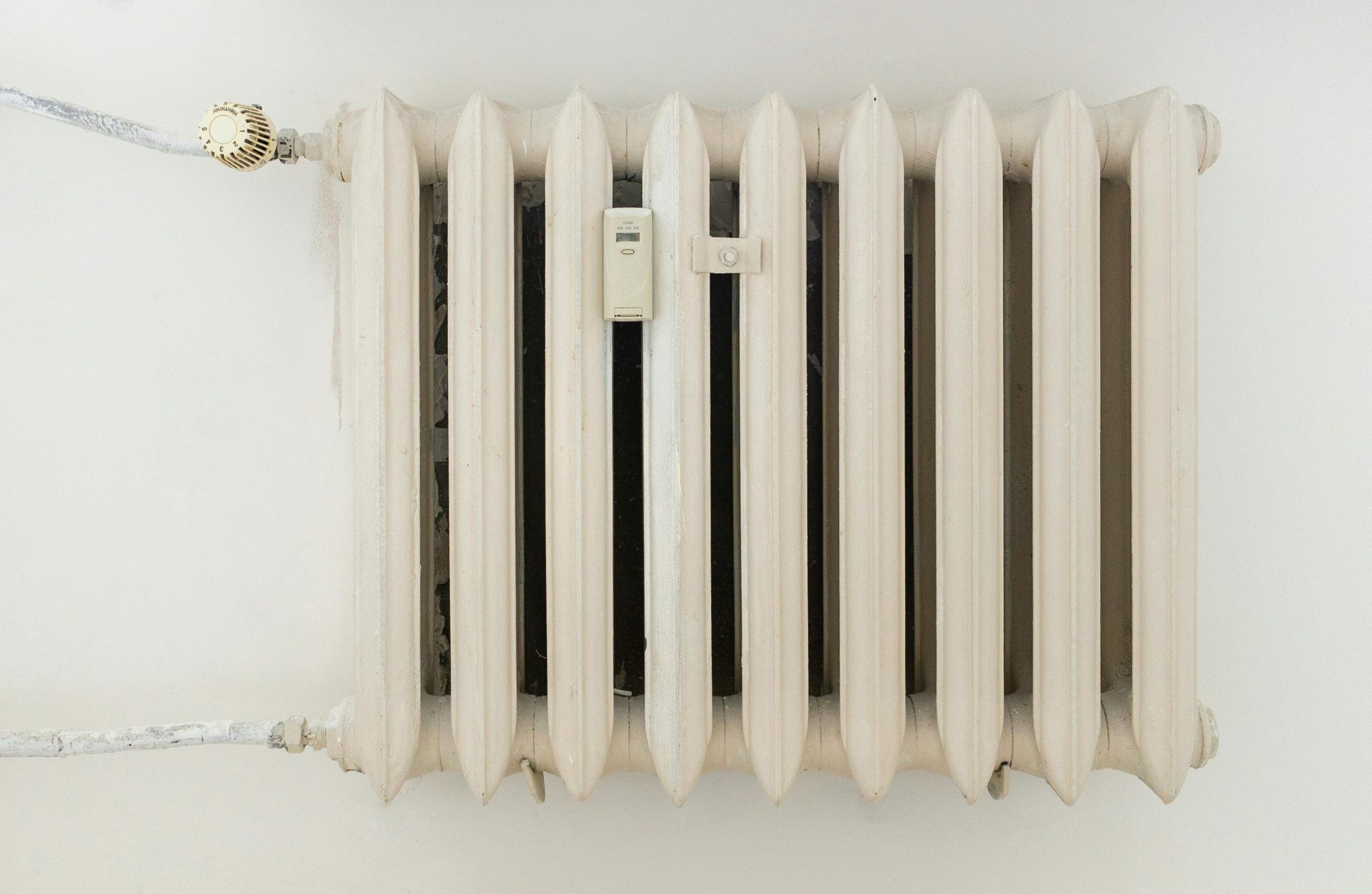 A classic white metal radiator on a plain wall, showcasing minimalist interior design. Un radiateur métallique blanc classique sur un mur uni, présentant un design d'intérieur minimaliste.