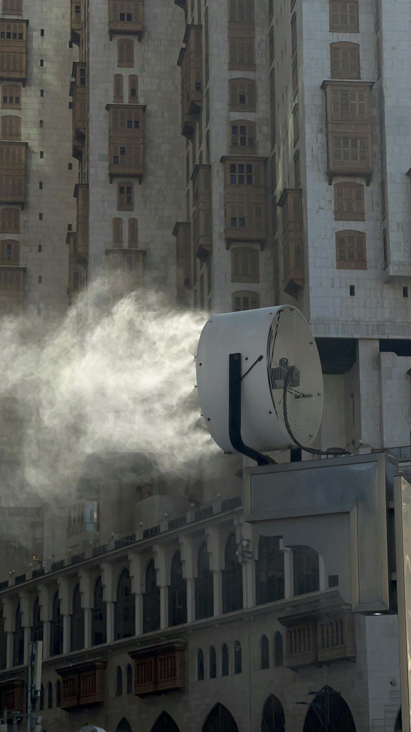A large industrial fan spraying mist against a backdrop of urban architecture. Un grand ventilateur industriel pulvérisant du brouillard sur un fond d'architecture urbaine.
