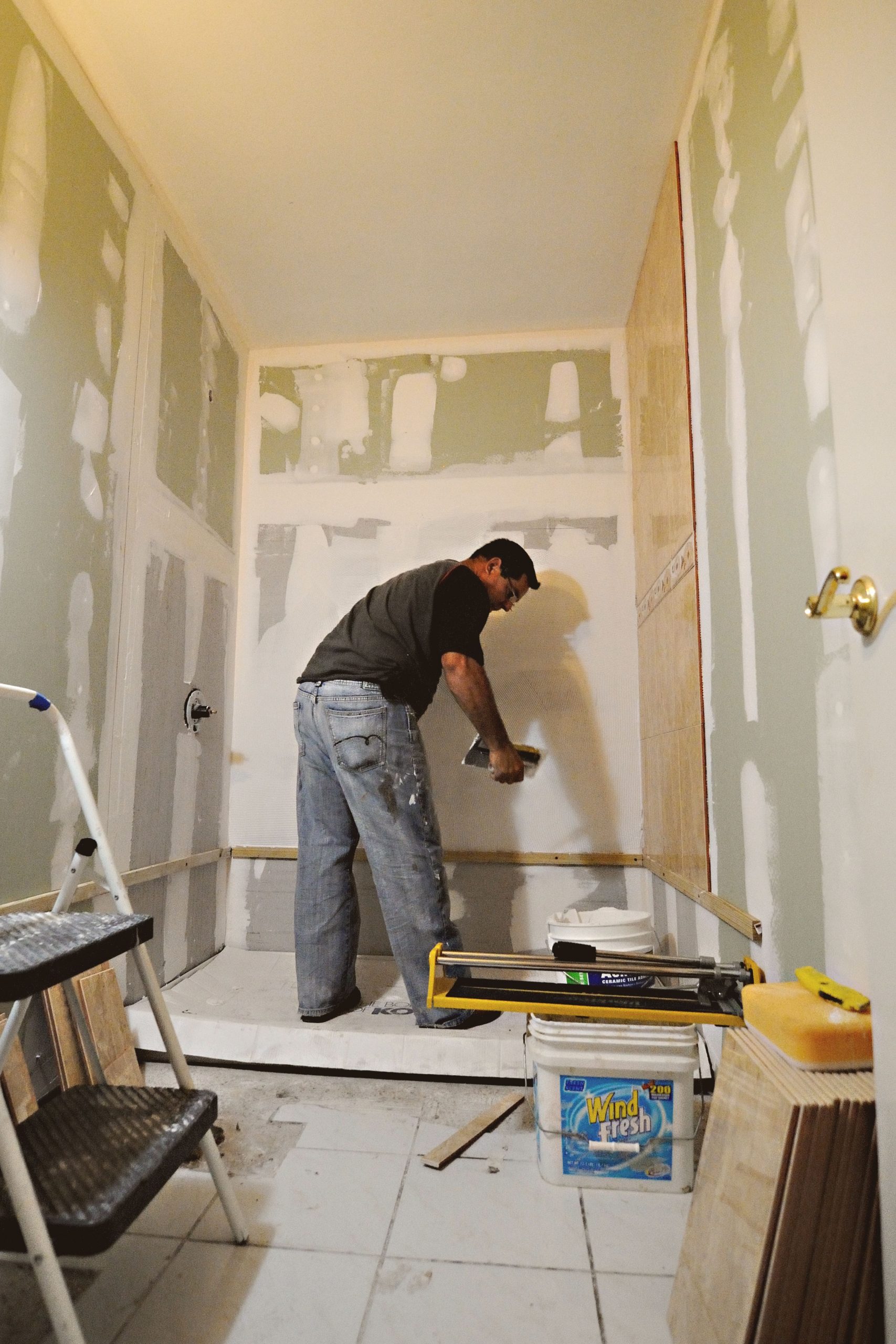 A man working on a bathroom renovation, applying drywall mud on interior walls. Un homme travaillant sur la rénovation d'une salle de bain, appliquant du composé à joints sur les murs intérieurs.