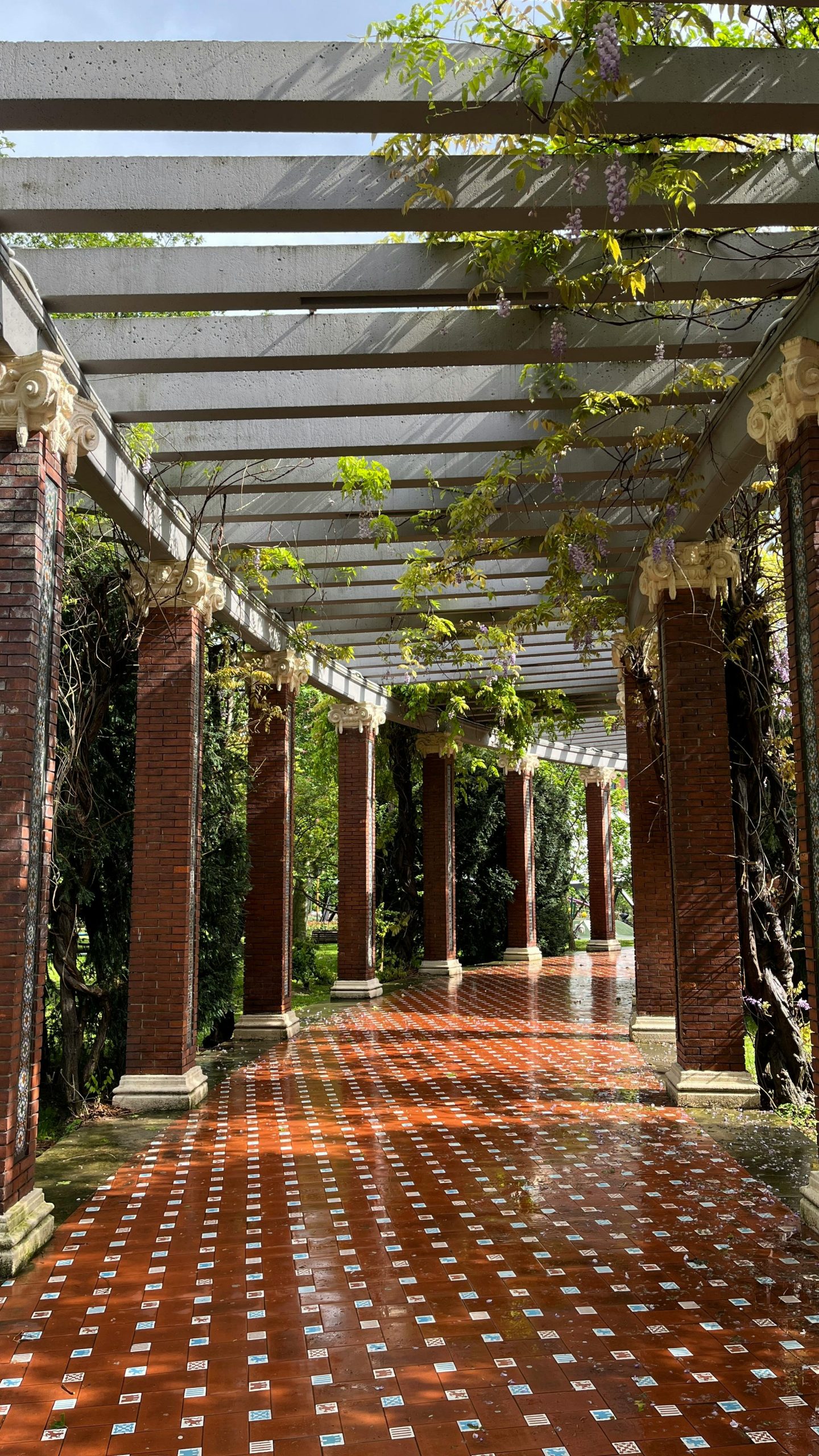A scenic outdoor colonnade with vibrant brick and lush foliage on a sunny day. Un colonnade extérieure pittoresque avec des briques vibrantes et un feuillage luxuriant par une journée ensoleillée.