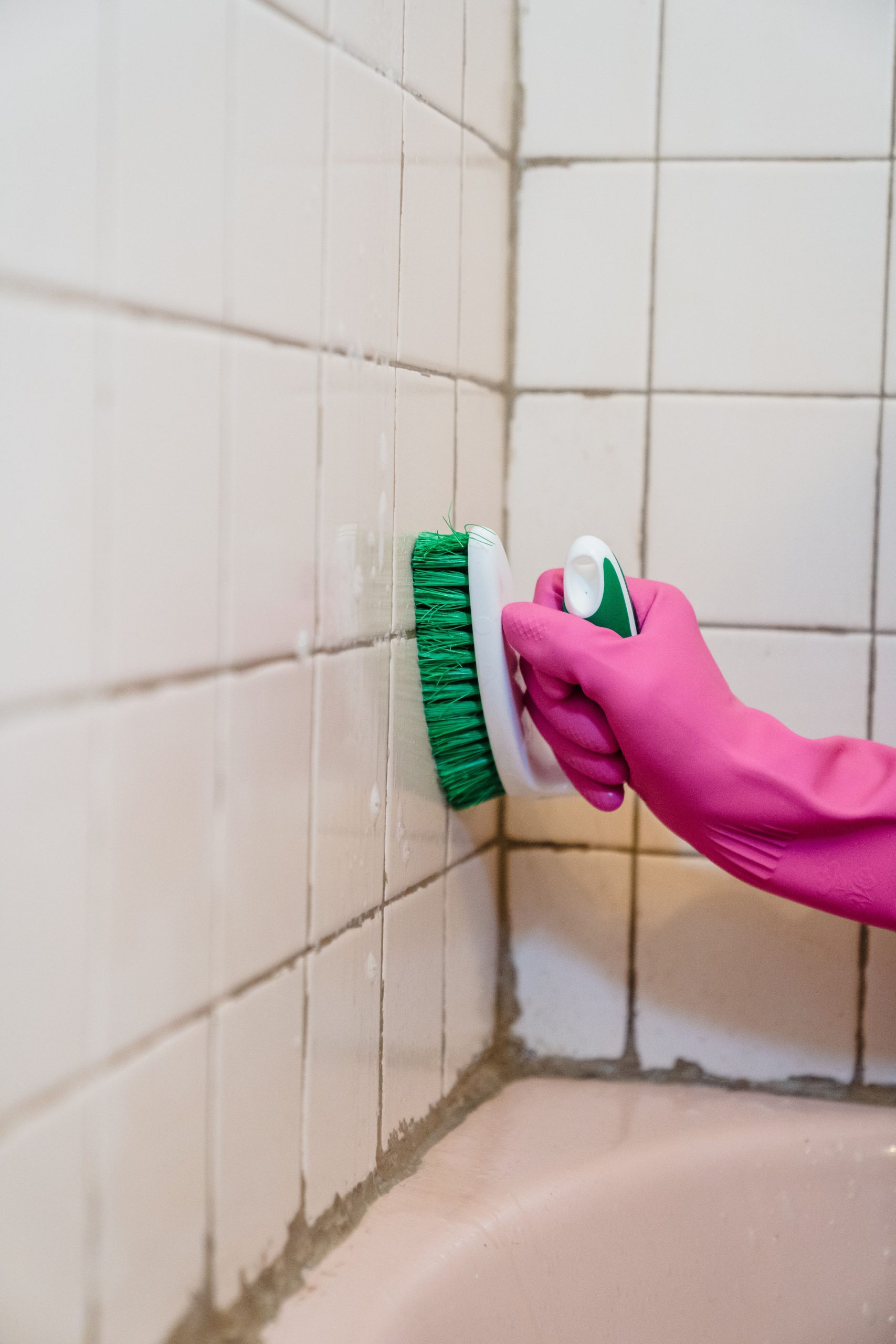 A person scrubs bathroom tiles wearing a pink glove, emphasizing cleanliness. Une personne frotte les carreaux de la salle de bain avec un gant rose, soulignant la propreté.