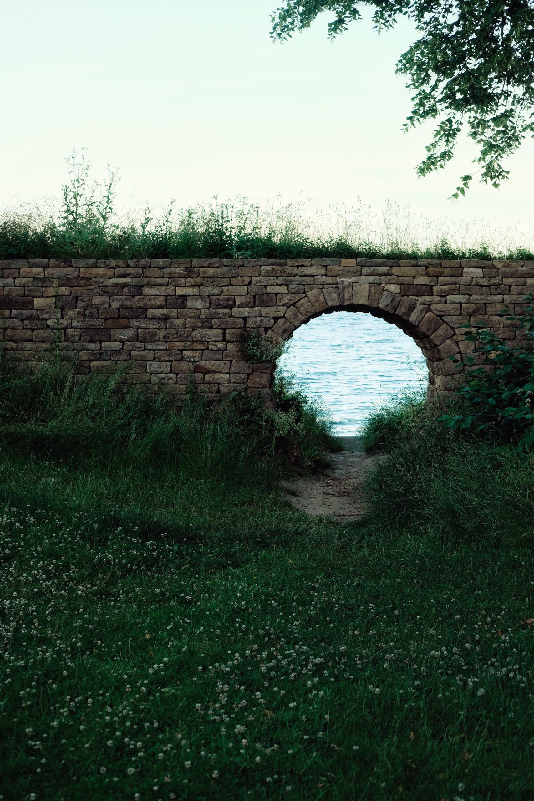 Tranquil scene of a brick archway open to a view of Denmark's shoreline with lush greenery. Scène tranquille d'une voûte en briques ouverte sur une vue du littoral du Danemark avec une végétation luxuriante.