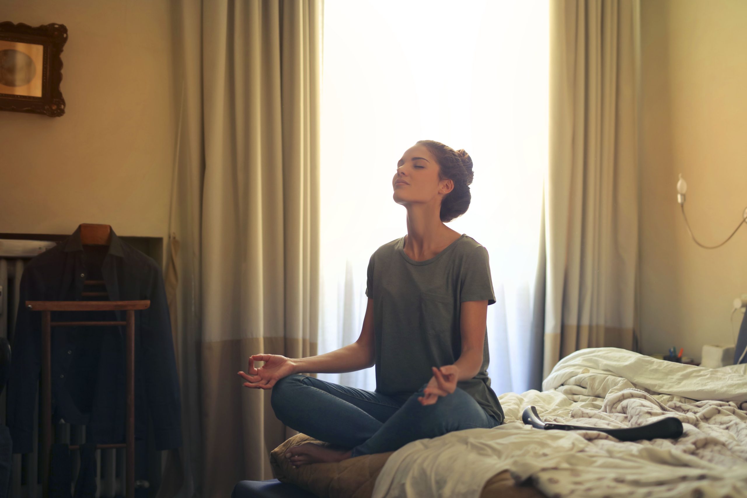 Adult woman practicing meditation on her bed surrounded by a calm bedroom atmosphere. Une femme adulte pratiquant la méditation sur son lit entourée d'une atmosphère calme de chambre à coucher.