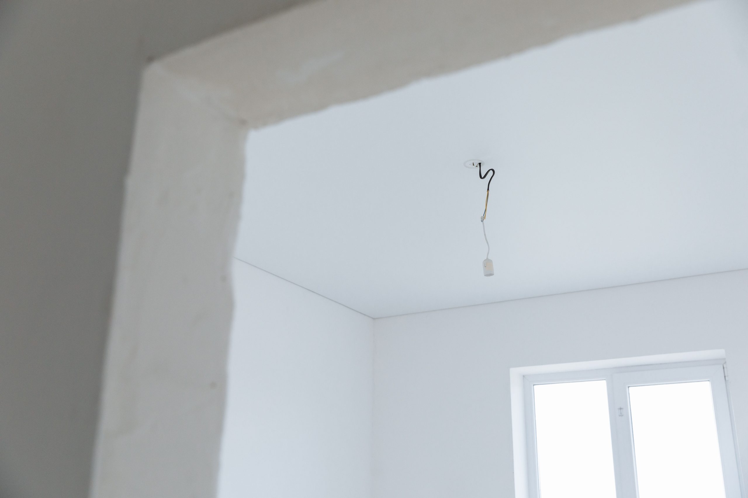 Bright white interior room with exposed electrical wiring and natural light. Pièce intérieure blanche et lumineuse avec câblage électrique apparent et lumière naturelle.
