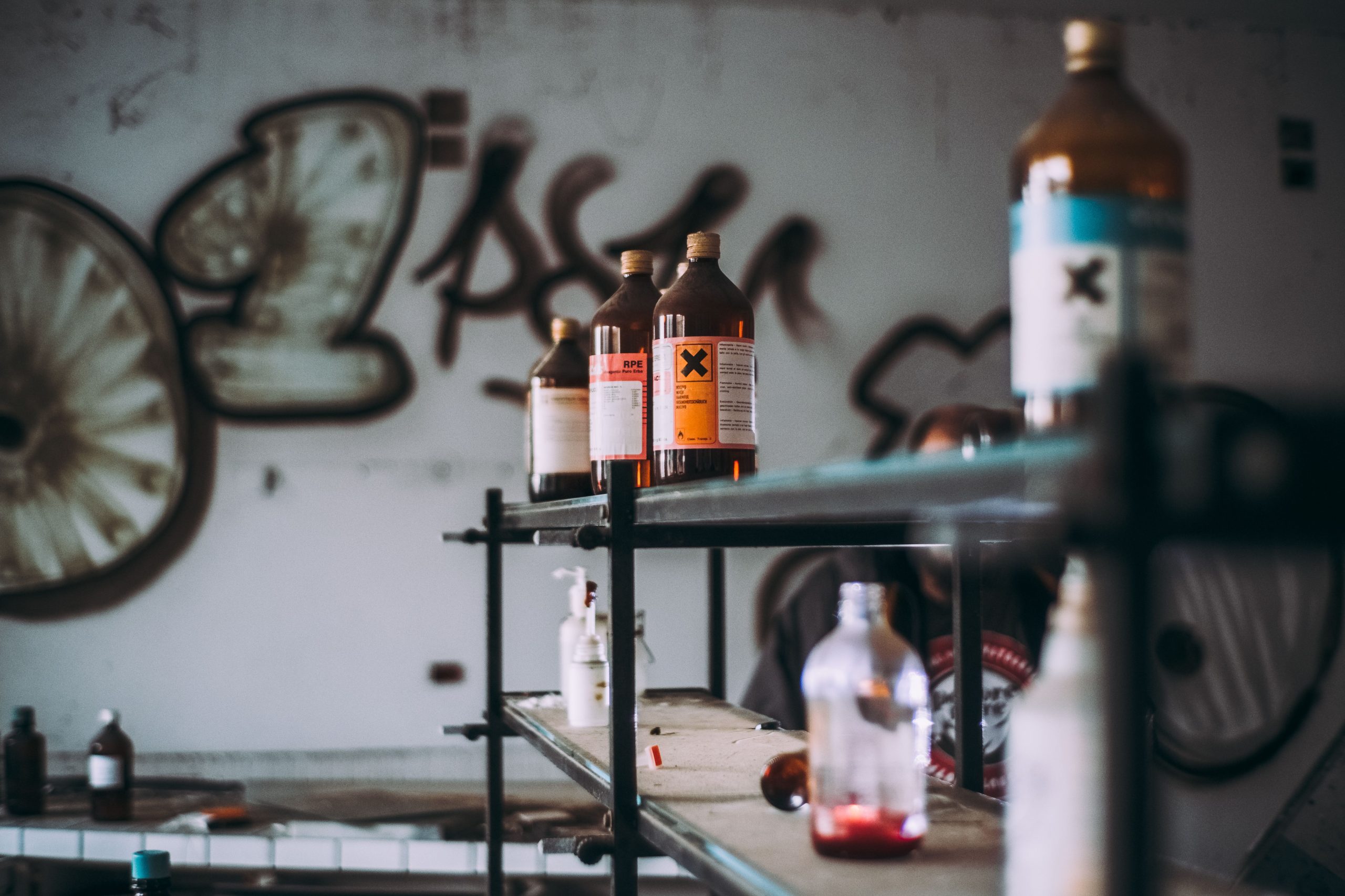 Découvrez une salle industrielle abandonnée avec des étagères de bouteilles de produits chimiques toxiques et des murs couverts de graffitis.
