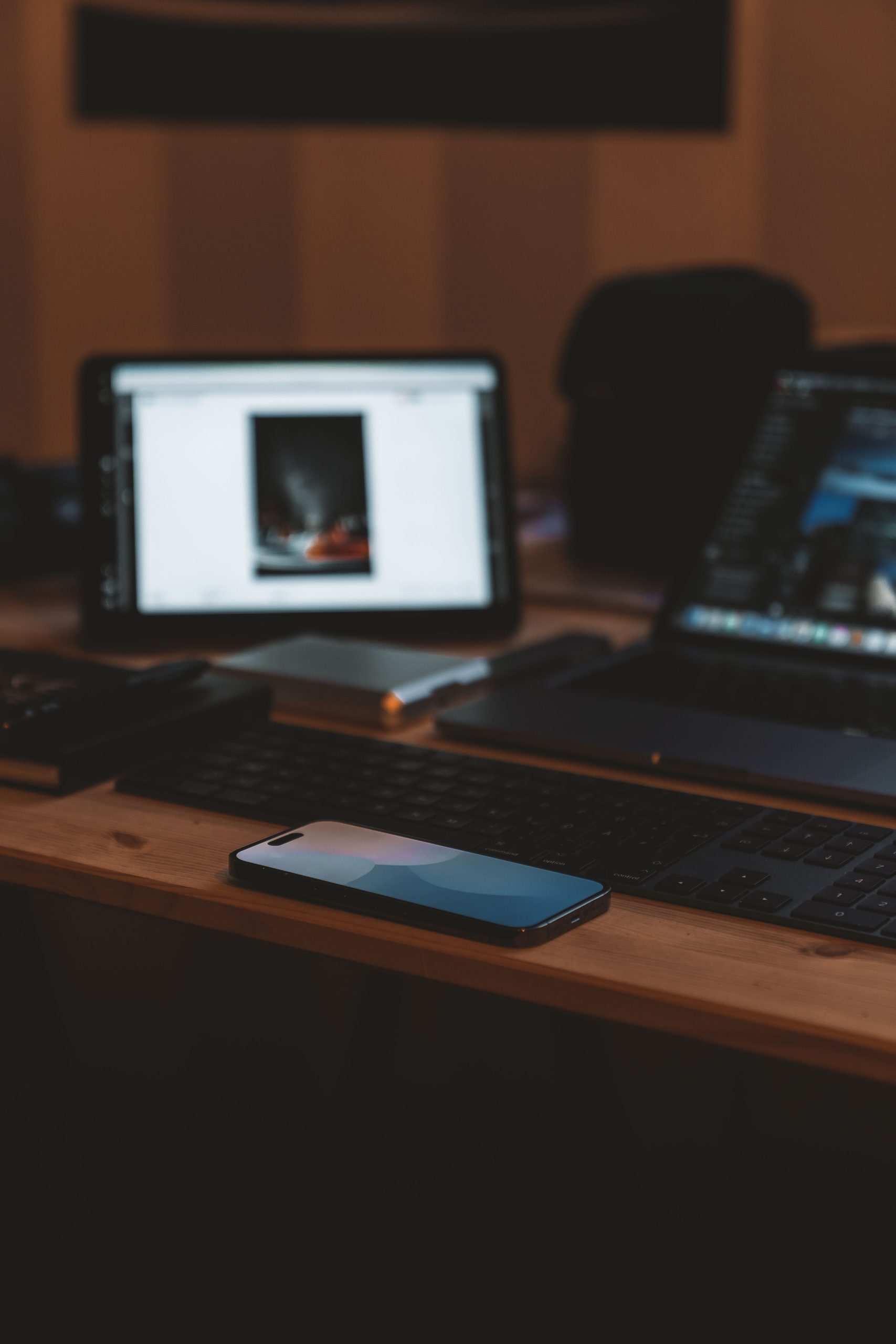 A cozy desk setup featuring a smartphone and laptop in a dimly lit office space. Un espace de travail confortable avec un smartphone et un ordinateur portable dans un bureau faiblement éclairé.