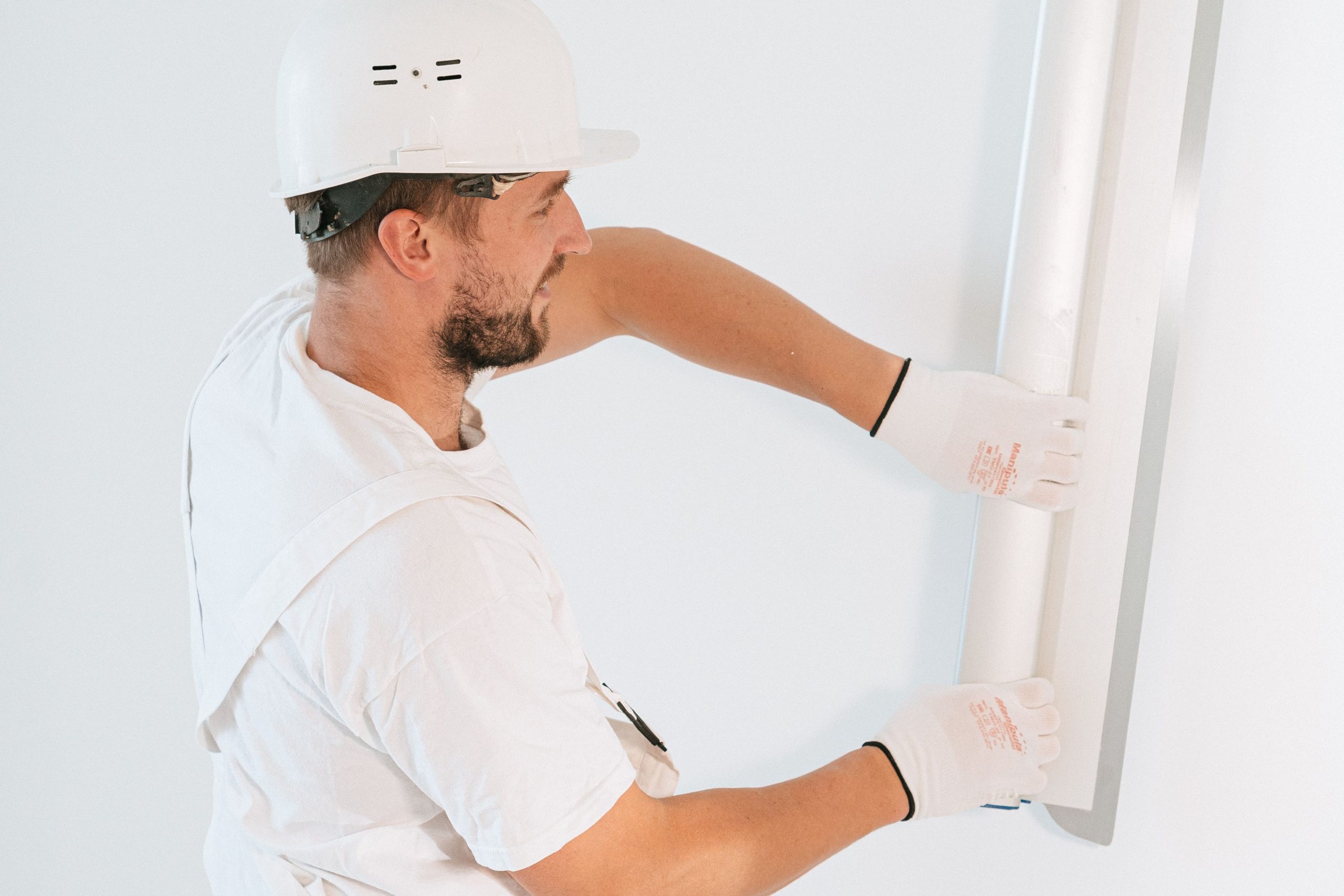Professional construction worker installing drywall with gloves and helmet inside a building. Ouvrier de construction professionnel installant des cloisons sèches avec gants et casque à l'intérieur d'un bâtiment.