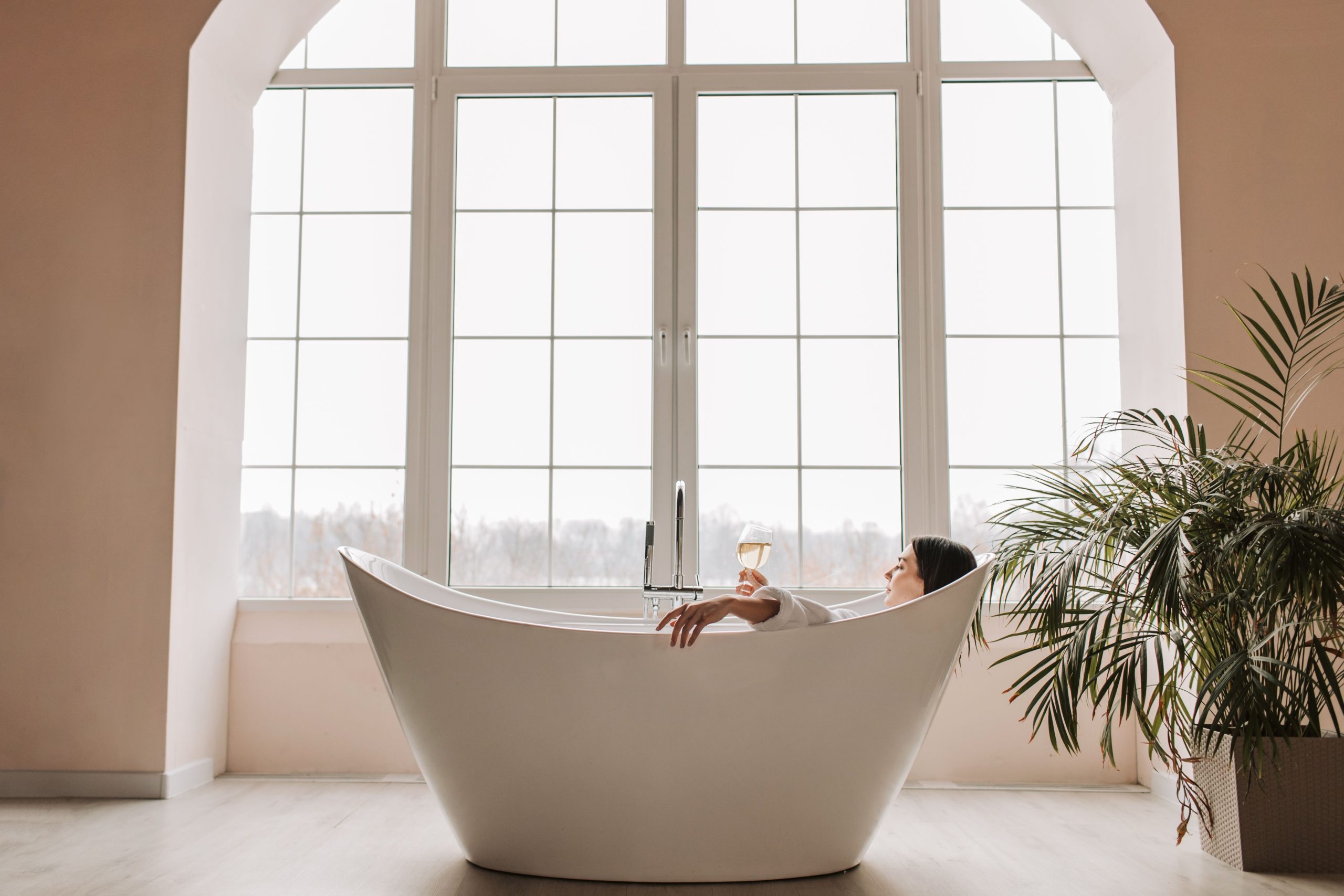 A serene scene of a woman enjoying a glass of wine while relaxing in a modern bathtub indoors. Une scène sereine d'une femme savourant un verre de vin en se détendant dans une baignoire moderne à l'intérieur.