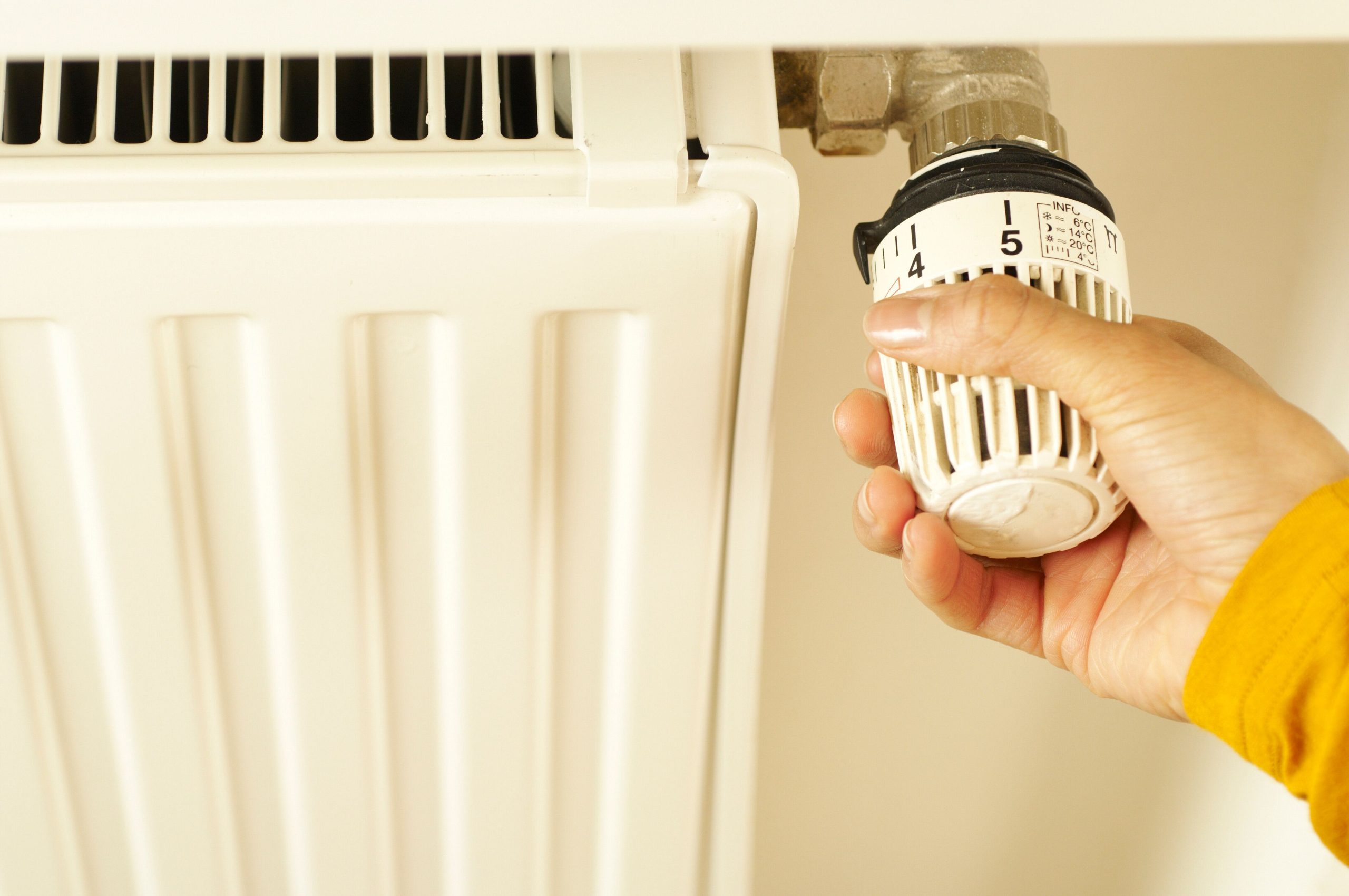 Close-up of hand adjusting radiator thermostat to control home heating temperature. Gros plan sur une main ajustant le thermostat du radiateur pour contrôler la température de chauffage de la maison.