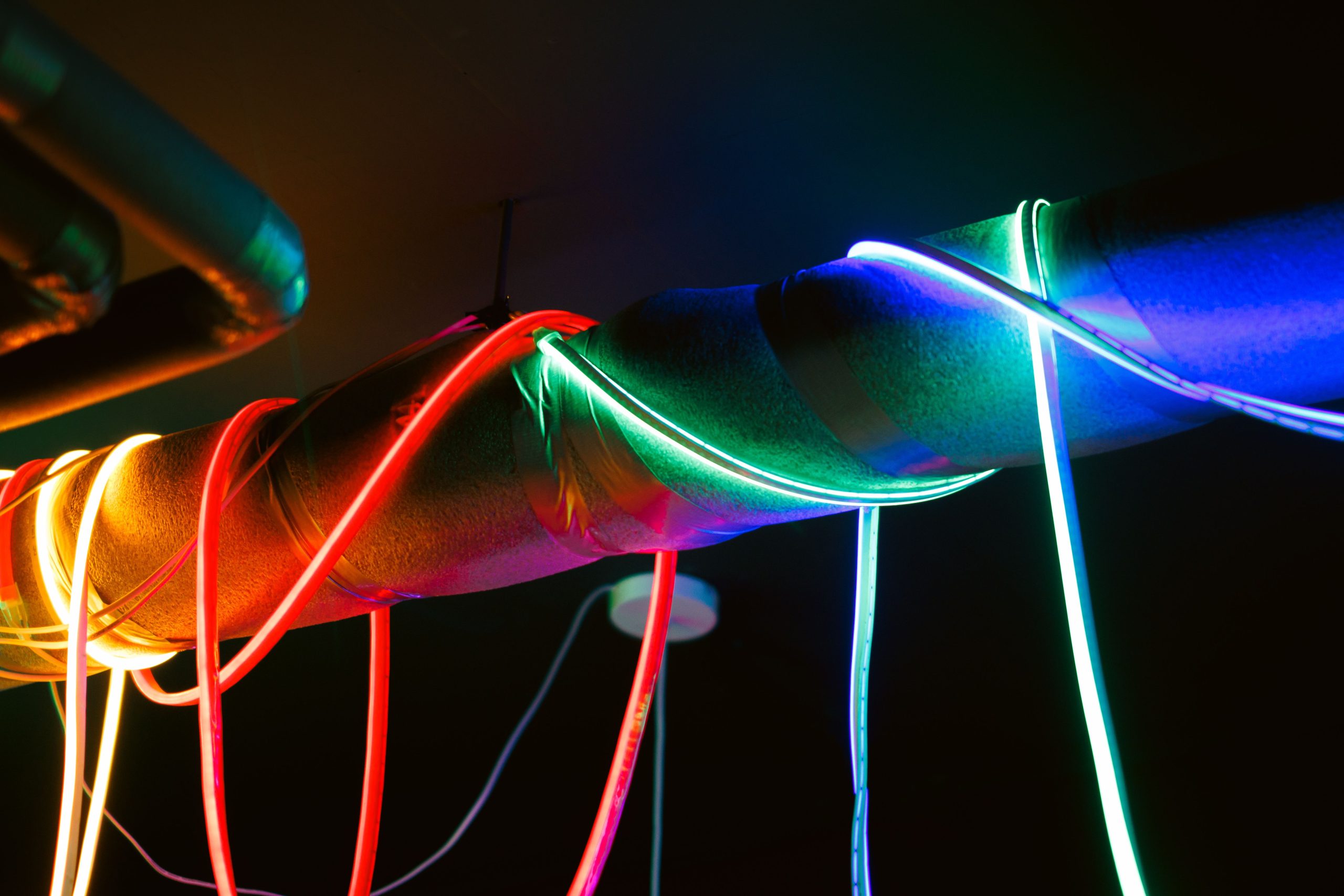 Vibrant LED lights in red, blue, and green illuminating a metal pipe in a dark room. Des lumières LED vibrantes en rouge, bleu et vert illuminant un tuyau métallique dans une pièce sombre.
