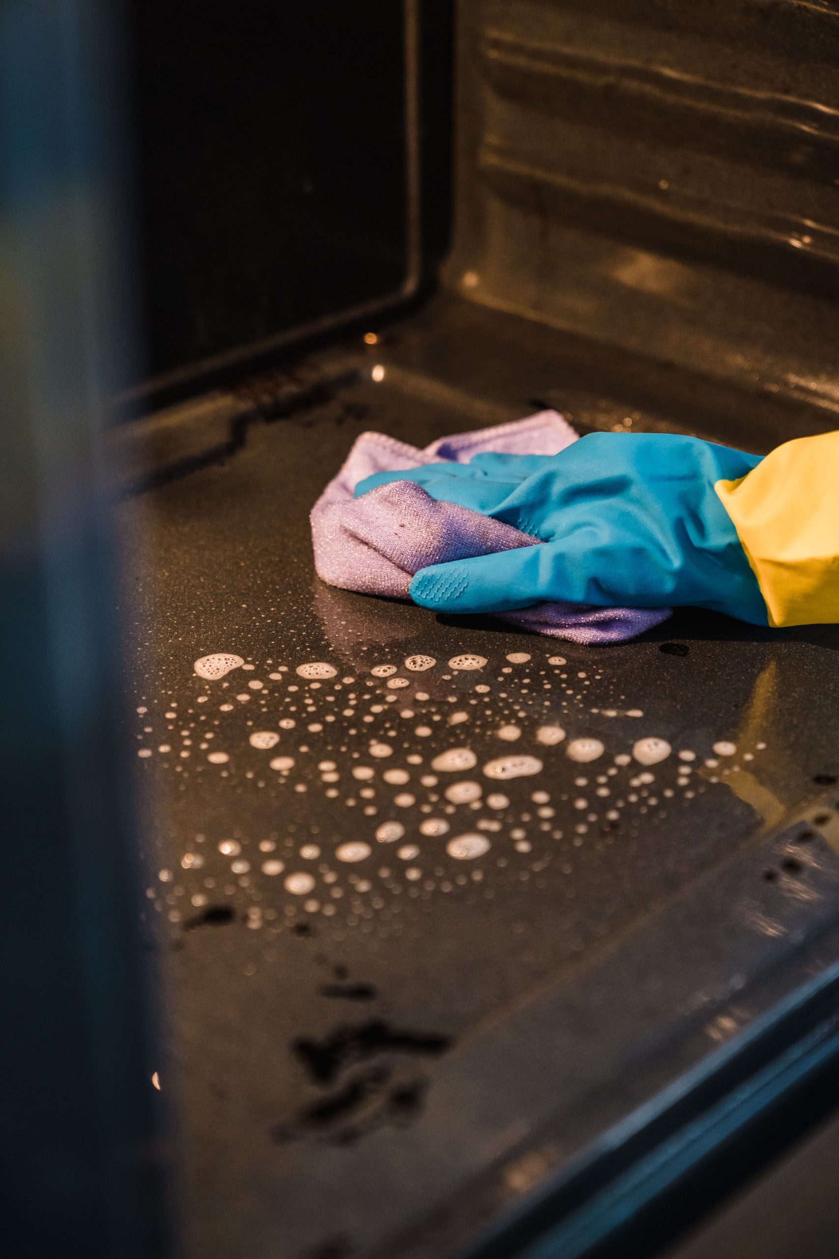 A gloved hand cleans an oven interior using a soapy cloth for a spotless finish. Une main gantée nettoie l'intérieur d'un four avec un chiffon savonneux pour un résultat impeccable.