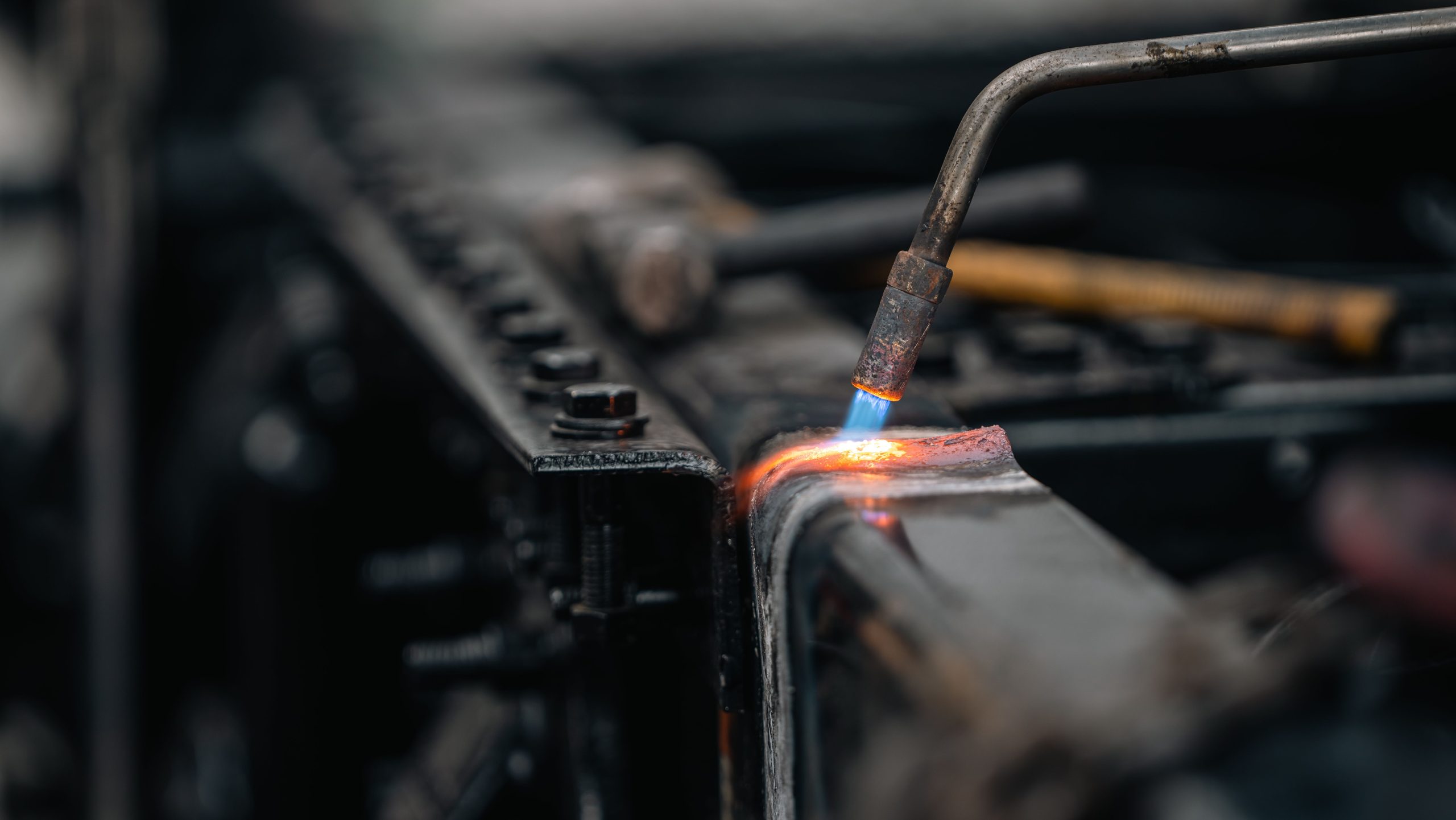 Detailed view of torch welding metal surface, featuring blue flame. Vue détaillée d'une surface métallique soudée à la torche, mettant en évidence une flamme bleue.