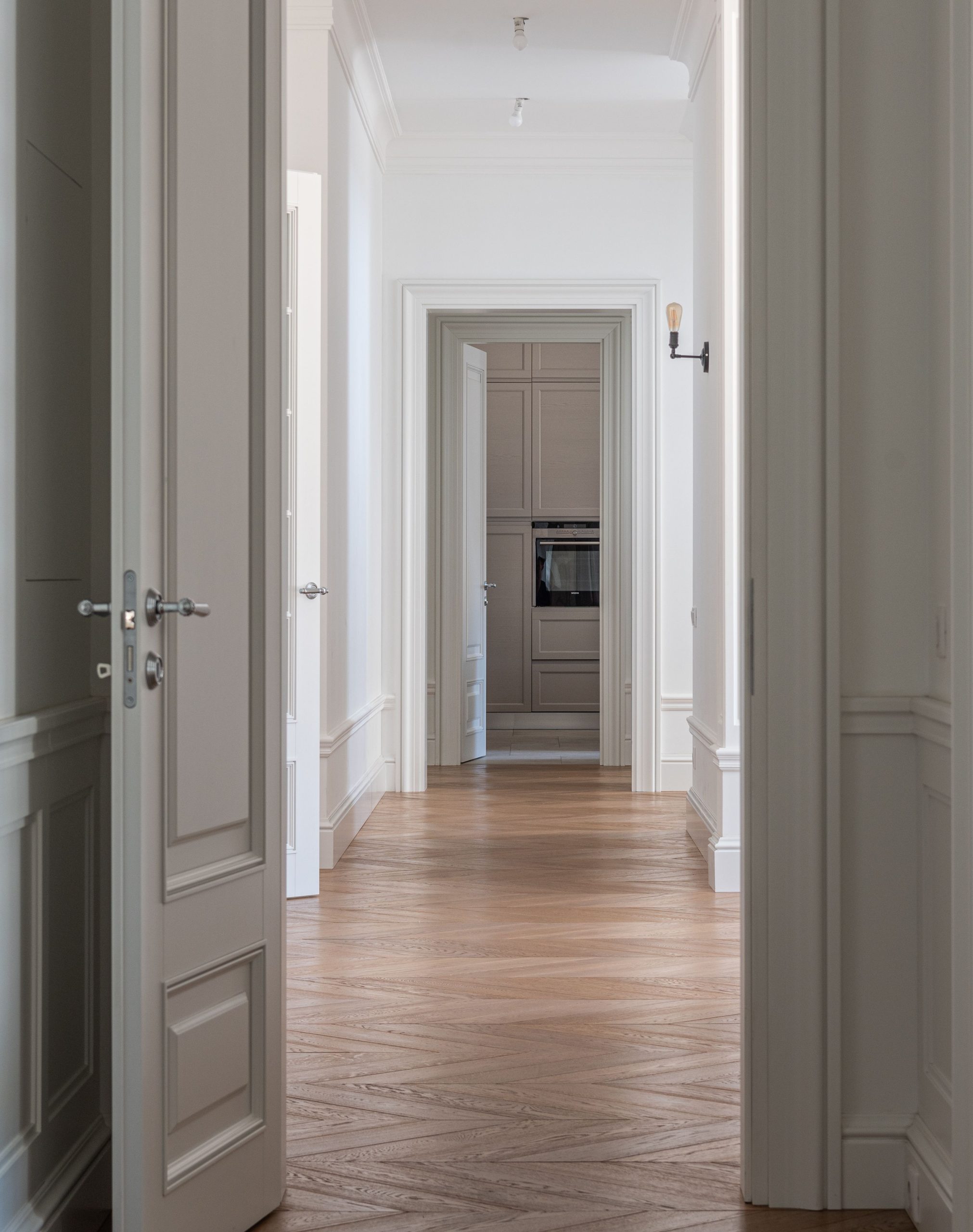 Couloir lumineux avec parquet en bois et murs blancs menant à une pièce avec placards intégrés.