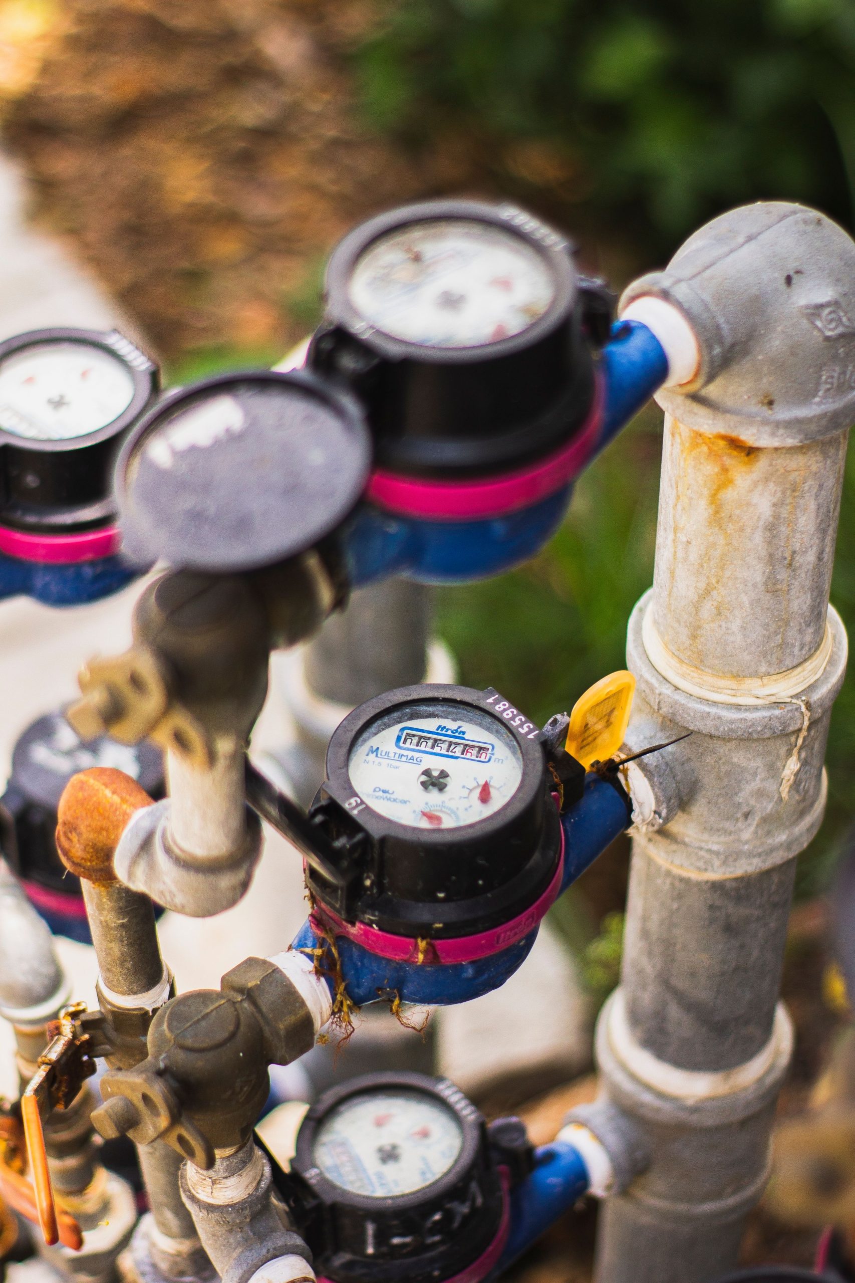 A detailed view of multiple water meters connected by pipes in an industrial setting. Une vue détaillée de plusieurs compteurs d'eau connectés par des tuyaux dans un environnement industriel.