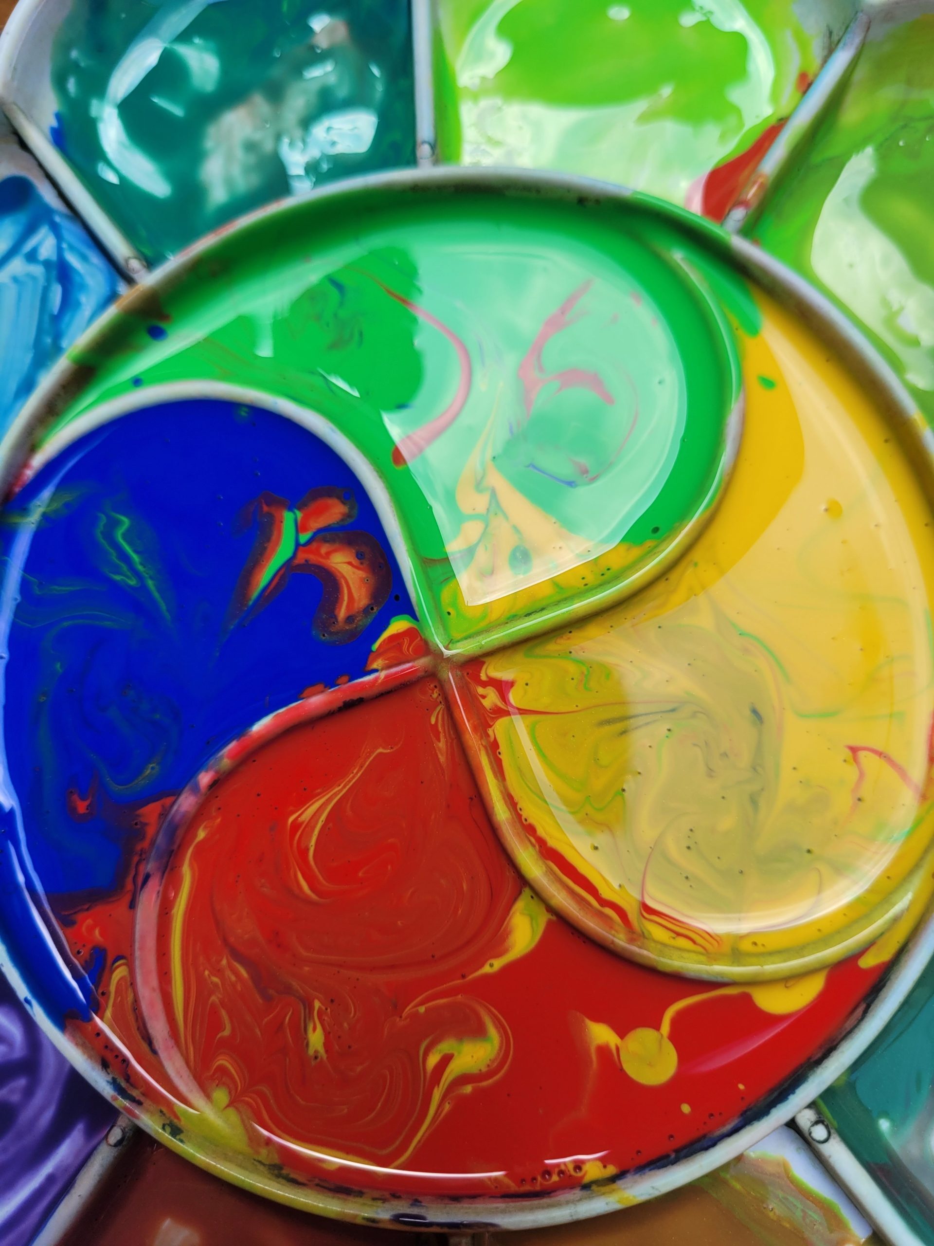 Close-up of vibrant paint swirls in a circular art palette, showcasing colorful patterns. Gros plan des tourbillons de peinture vibrants dans une palette d'art circulaire, mettant en évidence des motifs colorés.