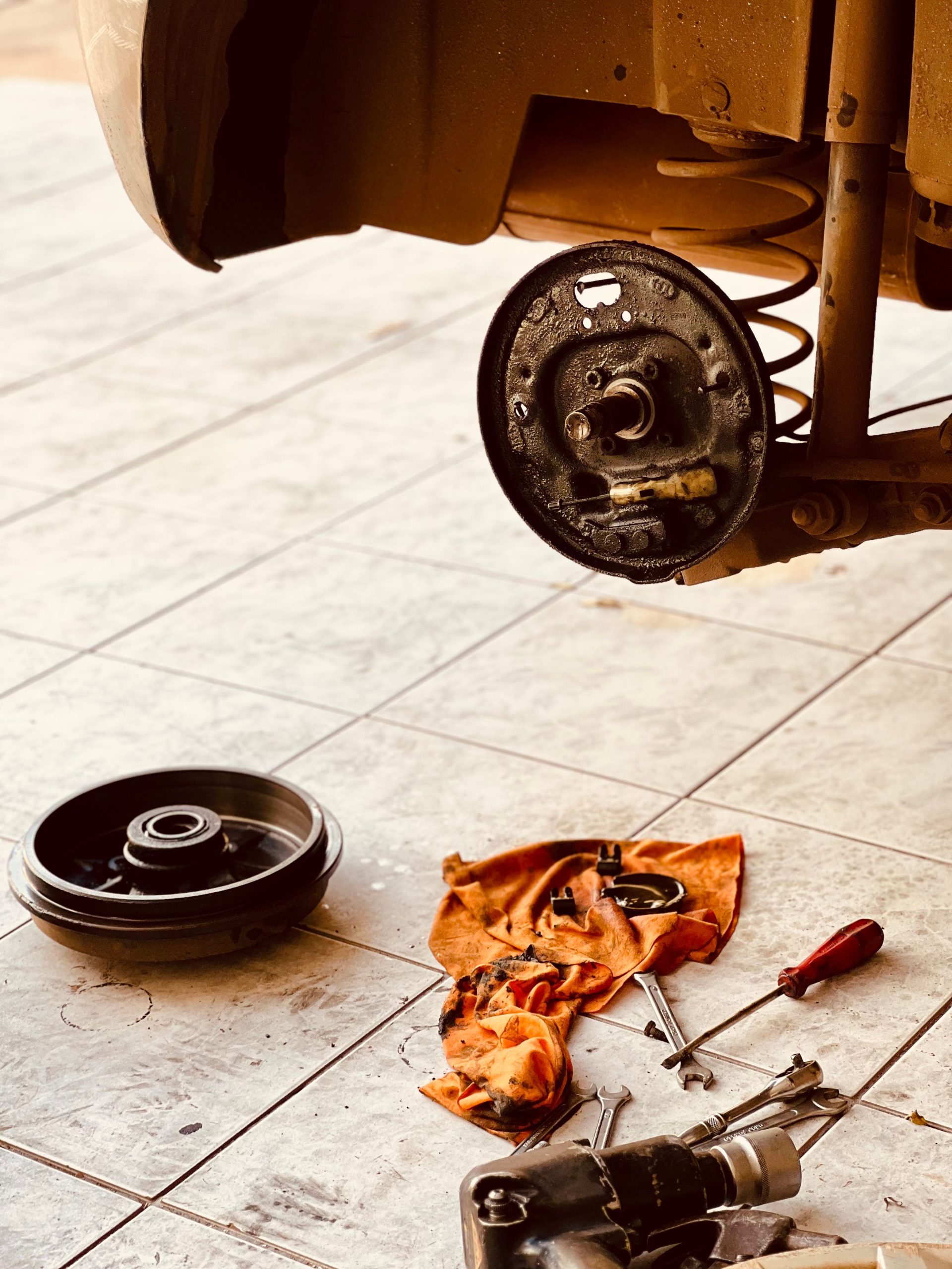 Close-up of a dismantled car brake rotor and tools on a garage floor, illustrating auto repair. Gros plan sur un rotor de frein de voiture démonté et des outils sur le sol d'un garage, illustrant la réparation automobile.