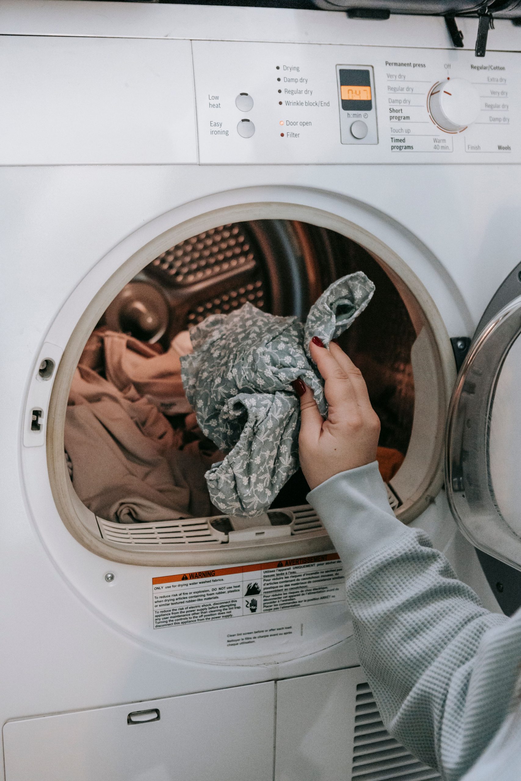 Femme méconnaissable chargeant des vêtements sales dans une machine à laver moderne blanche tout en faisant sa routine ménagère dans une pièce lumineuse à la maison