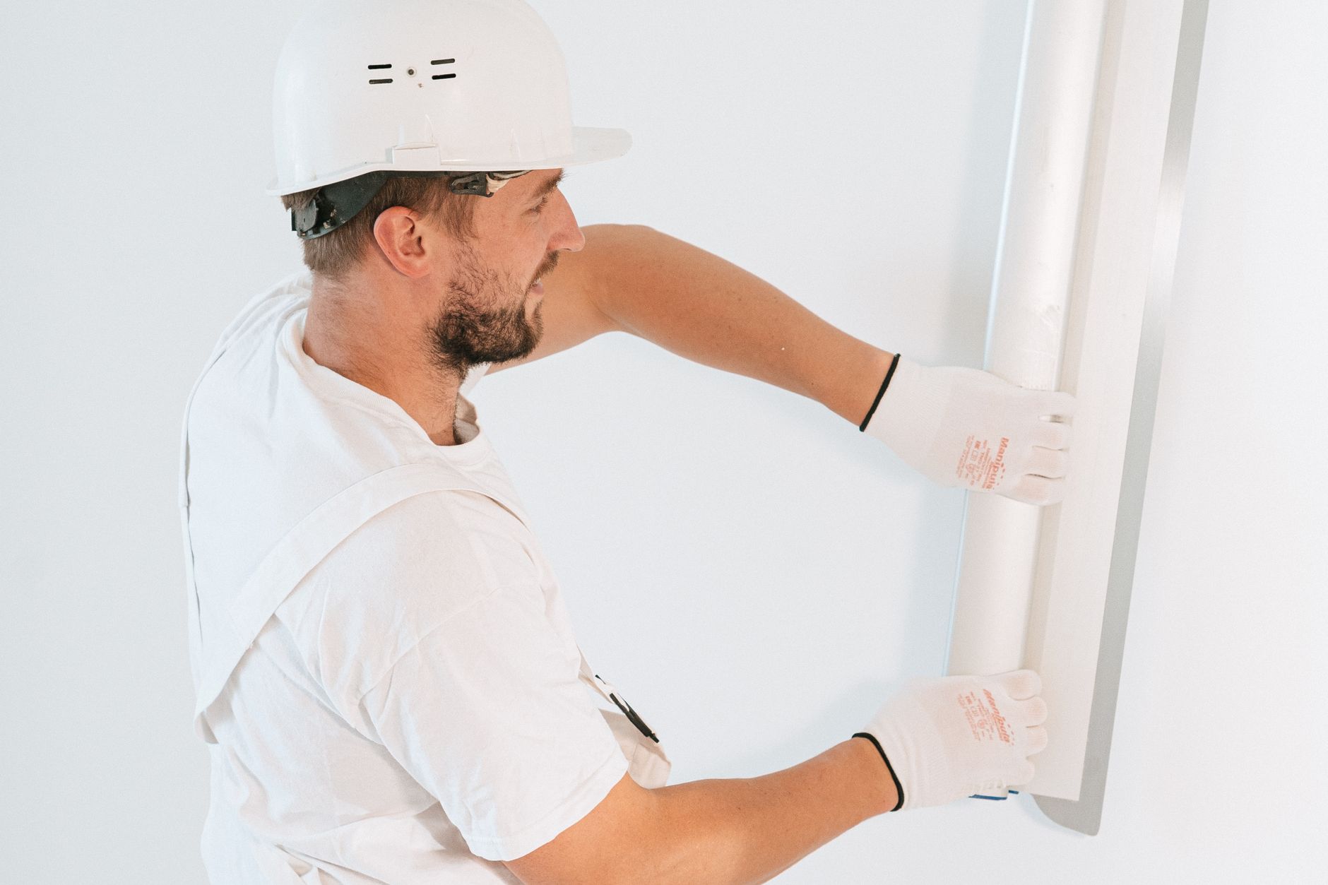 Plaquiste ganté qui présente une plaque de plâtre contre le plafond