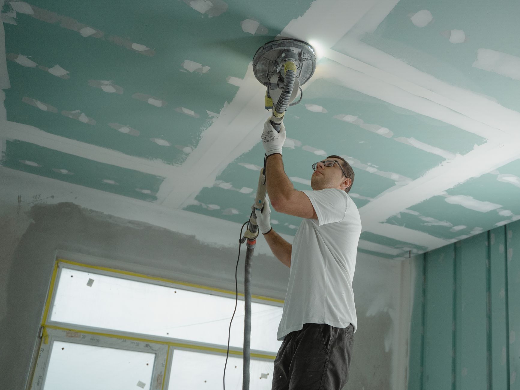 Ouvrier qui ponce un plafond en plaques de plâtre pendant une rénovation